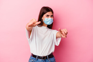 Young caucasian woman wearing a mask for virus isolated on pink background cheerful smiles pointing to front.