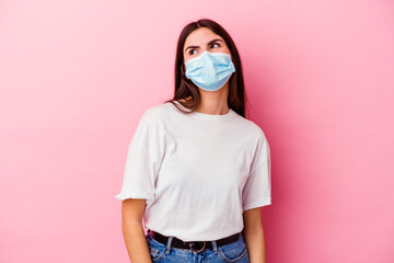 Young caucasian woman wearing a mask for virus isolated on pink background dreaming of achieving goals and purposes