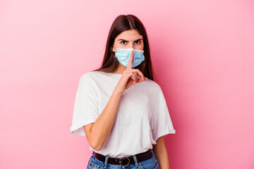 Young caucasian woman wearing a mask for virus isolated on pink background keeping a secret or asking for silence.