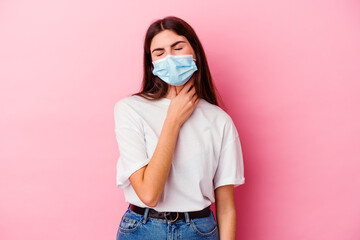 Young caucasian woman wearing a mask for virus isolated on pink background suffers pain in throat...