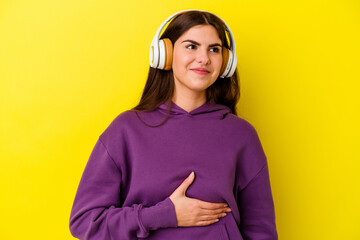 Young caucasian woman listening to music with headphones isolated on pink background touches tummy, smiles gently, eating and satisfaction concept.