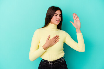Fototapeta premium Young caucasian woman isolated on blue background taking an oath, putting hand on chest.