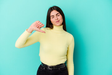 Young caucasian woman isolated on blue background showing a dislike gesture, thumbs down....