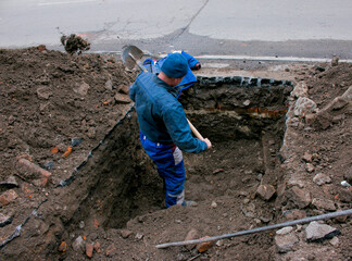 A man handyman digs a trench in the winter in the city by hand with a shovel. Construction...