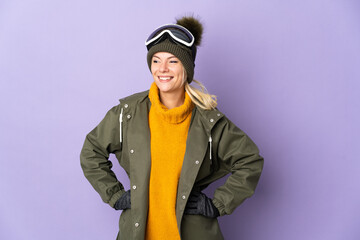 Skier Russian girl with snowboarding glasses isolated on purple background posing with arms at hip and smiling