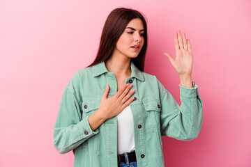 Young caucasian woman isolated on pink background taking an oath, putting hand on chest.