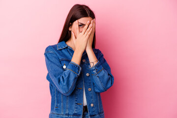 Young caucasian woman isolated on pink background blink through fingers frightened and nervous.