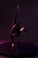 Graceful woman doing gymnastic exercise near pole in darkness