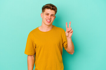 Fototapeta premium Young caucasian man isolated on blue background showing victory sign and smiling broadly.