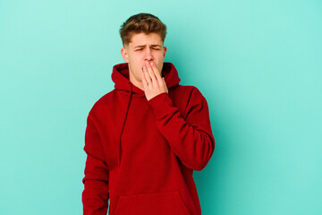 Young caucasian man isolated on blue background yawning showing a tired gesture covering mouth with hand.