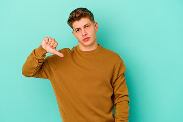 Young caucasian man isolated on blue background showing a dislike gesture, thumbs down....