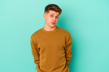 Young caucasian man isolated on blue background shrugs shoulders and open eyes confused.