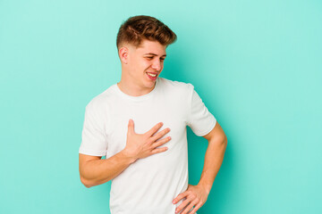 Young caucasian man isolated on blue background laughing keeping hands on heart, concept of happiness.