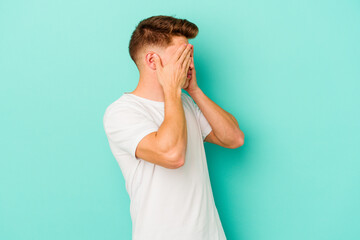 Young caucasian man isolated on blue background afraid covering eyes with hands.