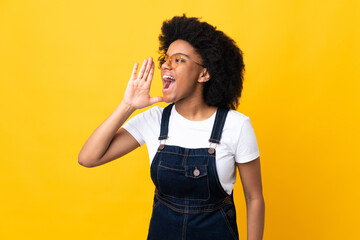 Young African American woman isolated on yellow background shouting with mouth wide open to the side