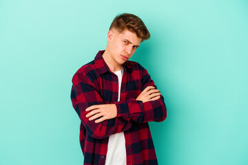 Young caucasian man isolated on blue background frowning face in displeasure, keeps arms folded.