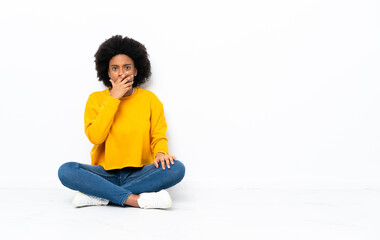 Young African American woman sitting on the floor surprised and shocked while looking right