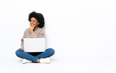 Young African American woman with a laptop sitting on the floor smiling