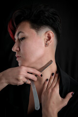 Half-length portrait of young adult barber woman on black background holding vintage straight razor, modern barber girl concept