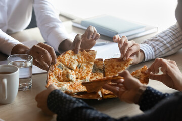 Crop close up of diverse colleagues friends share eat delicious pizza on work break in office together. Multiracial employees have tasty lunch dinner at workplace, enjoy Italian fast food or snack.
