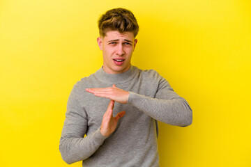 Young caucasian man isolated on yellow background showing a timeout gesture.