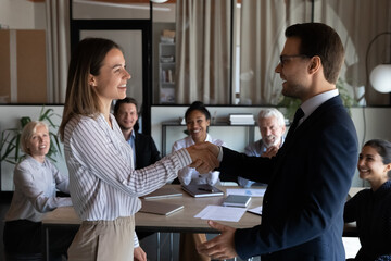 Happy Caucasian businessman shake hand of smiling female employee worker congratulate greet with job promotion. Excited diverse businesspeople colleagues handshake get acquainted at meeting.