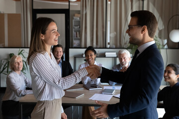 Happy Caucasian businessman shake hand of smiling female employee worker congratulate greet with...