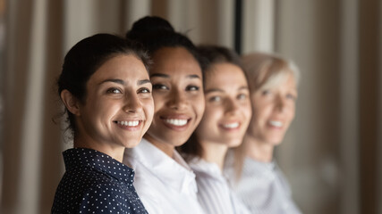 Fototapeta premium Smiling diverse multiracial female employees workers show team unity and leadership at workplace. Happy multiethnic women colleagues coworkers feel motivated in office. Success, recruitment concept.