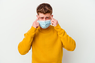 Young man wearing a mask for coronavirus isolated on white background focused on a task, keeping forefingers pointing head.