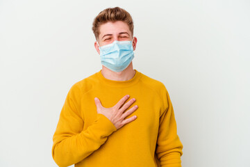 Young man wearing a mask for coronavirus isolated on white background laughs out loudly keeping hand on chest.