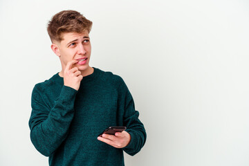 Young caucasian blonde man using a telephone isolated on white background relaxed thinking about something looking at a copy space.