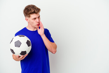 Young caucasian man playing soccer isolated on background is saying a secret hot braking news and looking aside