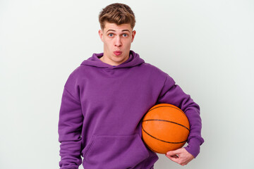 Young caucasian man playing basketball isolated background shrugs shoulders and open eyes confused.