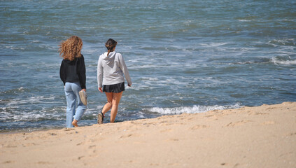 Duas amigas a caminhar na praia junto do mar num dia de primavera de sol