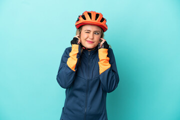 Young cyclist woman isolated on blue background frustrated and covering ears