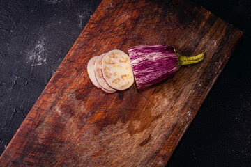 cutting purple eggplant with knife on wood