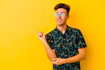 Young caucasian man wearing a Hawaiian shirt isolated on yellow background smiling cheerfully pointing with forefinger away.