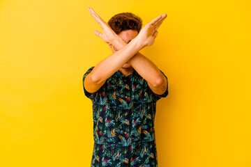 Young caucasian man wearing a Hawaiian shirt isolated on yellow background keeping two arms crossed, denial concept.