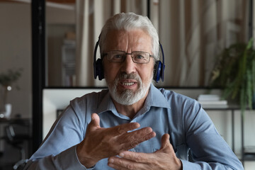 Headshot portrait screen view of middle-aged Caucasian male employee in headphones talk speak on...