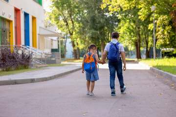 Cheerful schoolchildren, a little girl and a boy in a white shirt with backpacks go on the way to school.