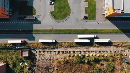 Large long truck drives along empty modern road past contemporary huge storehouse building on sunny autumn day bird eye view