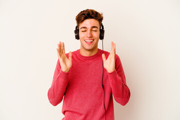 Young caucasian man listening to music isolated on white background joyful laughing a lot. Happiness concept.