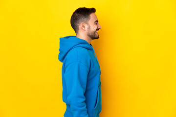 Young caucasian handsome man isolated on yellow background laughing in lateral position