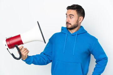 Young caucasian handsome man isolated on white background holding a megaphone with stressed expression