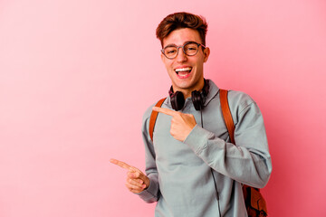 Young student man isolated on pink background pointing with forefingers to a copy space, expressing excitement and desire.