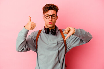 Young student man isolated on pink background showing thumbs up and thumbs down, difficult choose concept