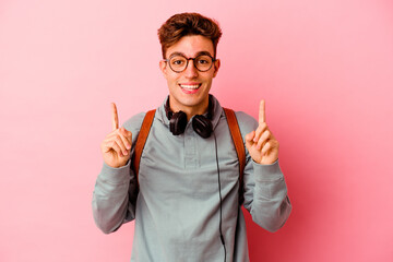 Young student man isolated on pink background indicates with both fore fingers up showing a blank...