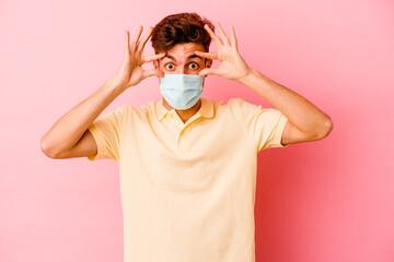 Young caucasian man wearing a protection for coronavirus isolated on pink background keeping eyes opened to find a success opportunity.