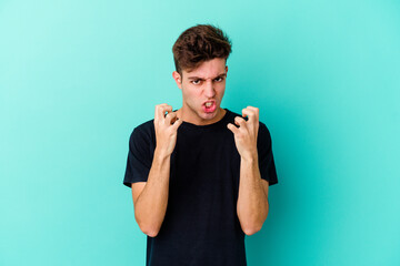 Young caucasian man isolated on blue background upset screaming with tense hands.
