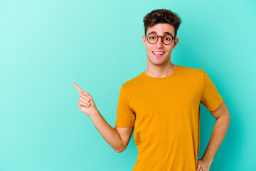 Young caucasian man isolated on blue background smiling cheerfully pointing with forefinger away.